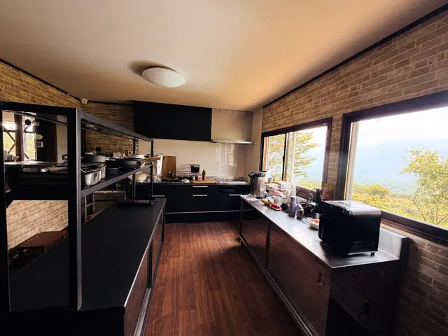 The shared kitchen after the rebuild — black cabinets and brick-pattern walls, steel prep tables, the valley in the corner window
