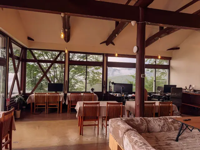 The work corner today — desks, monitors and office chairs at the window wall, mountains and cloud beyond the glass