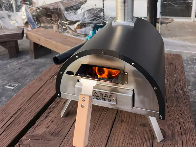 The KABUTO wood-fired pizza oven on a wooden table, a fire burning in its firebox