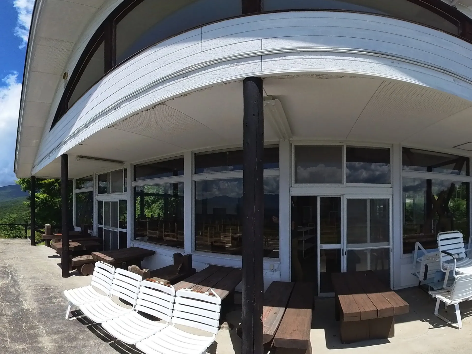 360° — August 2025, outside the resthouse: white loungers and wooden benches on the deck, mountains all around under a summer sky