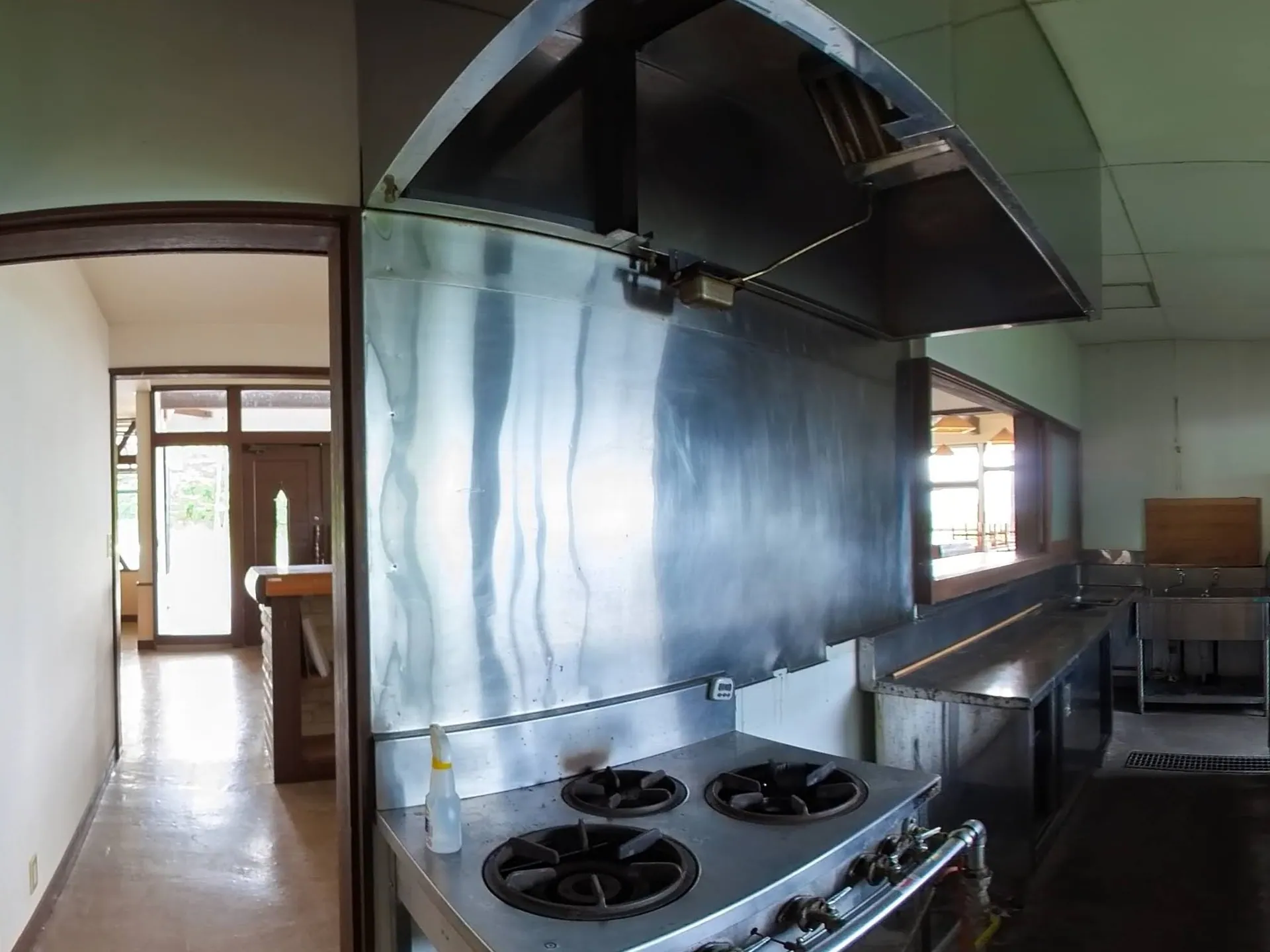 August 2025 — the old commercial kitchen: gas burners under a smoke-stained hood, steel counters, a dark floor