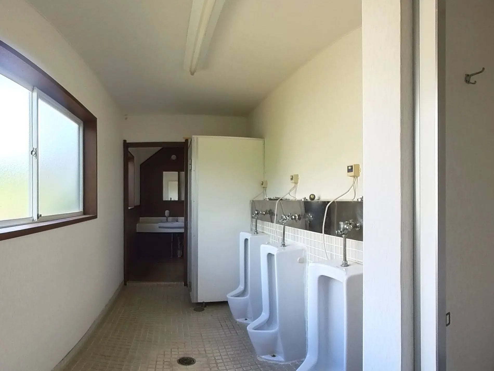 August 2025 — the washroom as we found it: bare walls, loose wiring above the urinals, old tile underfoot